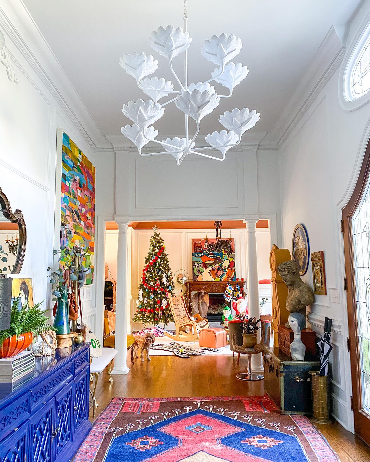 Christmas decor inspiration - a bright entryway with royal blue chest and blue and pink rug, a lit christmas tree in the back and a Stray Dog Designs Arlo Chandelier hanging.